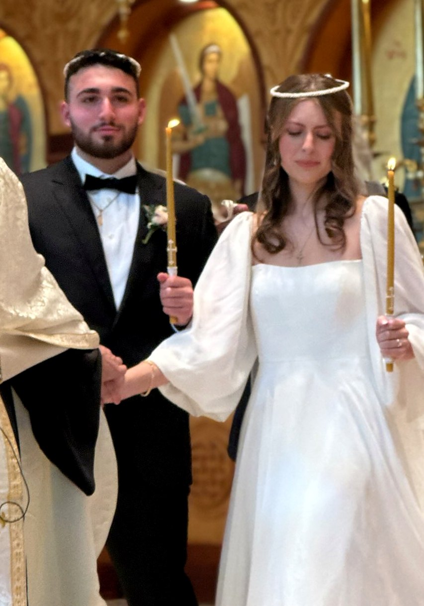 Nabil and his wife walking together during their Greek Orthodox wedding ceremony, each holding a candle